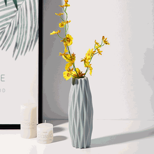 Diamond pattern faux ceramic vase with yellow flowers on white surface next to candles and framed artwork