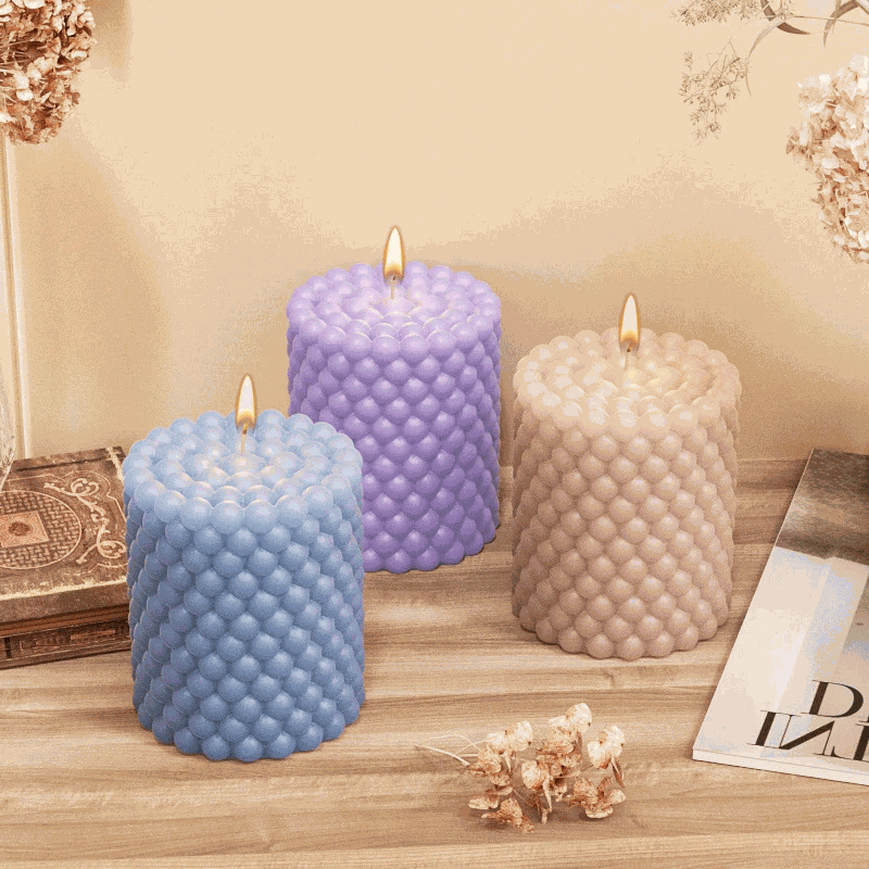 Three lit handmade bubble cube candles in blue, purple, and beige made with Bubble Bliss Candle Mold on wooden surface.