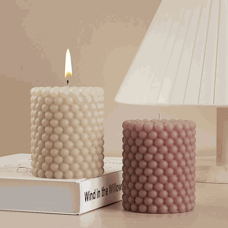 Two round bubble candles, one lit, showcasing unique textures beside a lamp and book.
