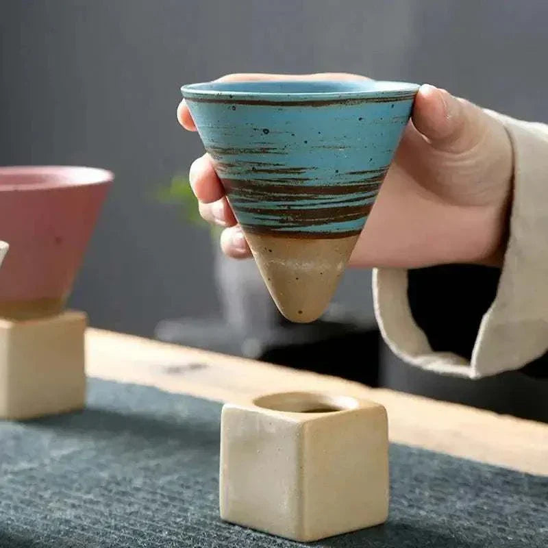 Hand holding a Japanese retro ceramic coffee cup with blue glaze and unique conical design on a wooden table.