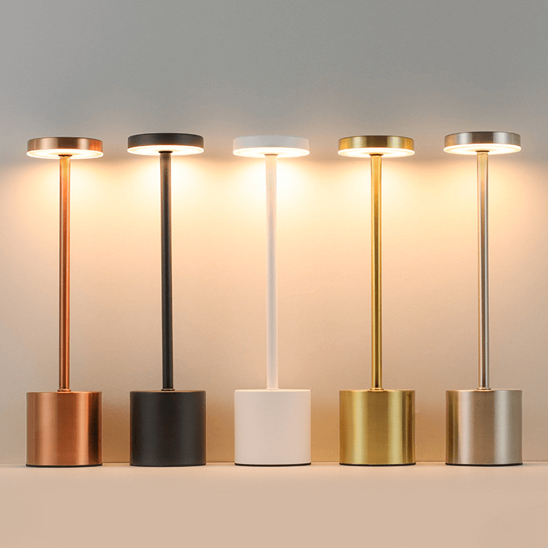 Showcasing five TouchGlow LED lamps in various finishes: copper, black, white, gold, and silver, providing warm illumination.