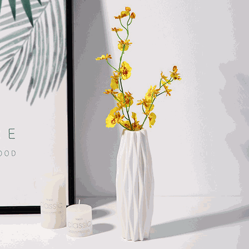 White diamond pattern faux ceramic vase with yellow flowers on table near candles and framed artwork