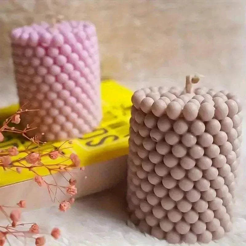 Round 3D bubble candles in pink and beige displayed with dried flowers on a yellow book.