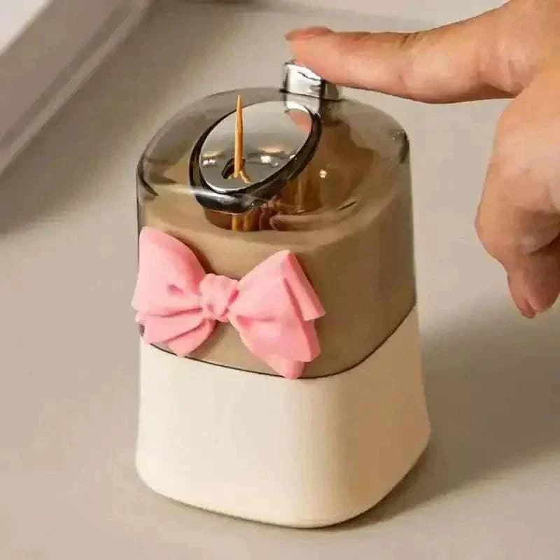 Stylish pop-up toothpick holder with pink bow, easy push-dispensing mechanism for organized toothpick storage.