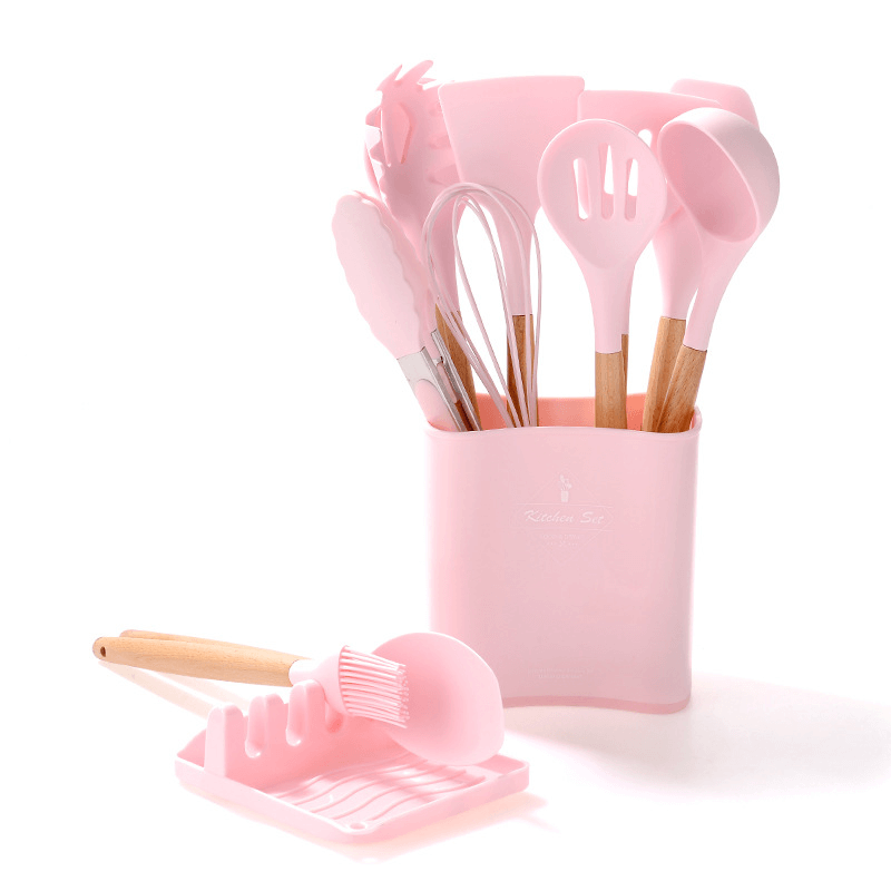 Silicone kitchen tools set with wooden handles in pink, featuring spatulas and utensils in a storage holder.