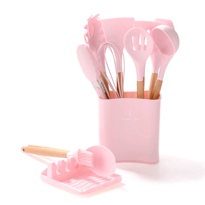 Silicone kitchen tools set with wooden handles in pink, featuring spatulas and utensils in a storage holder.