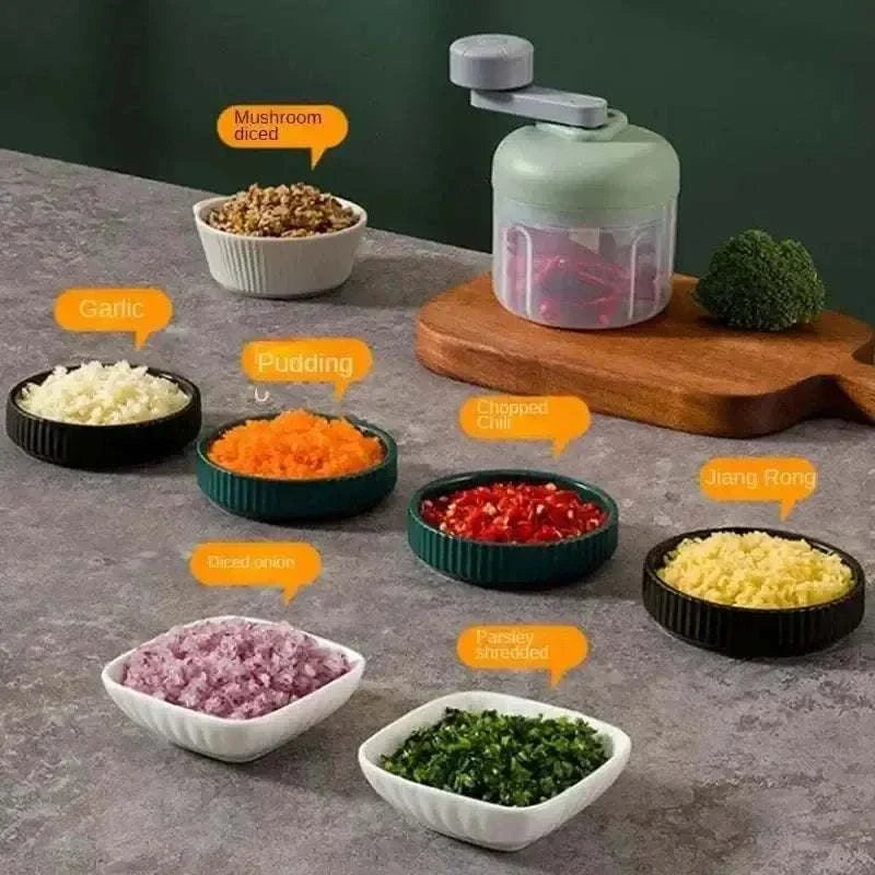 Compact hand-crank food chopper with diced vegetables including garlic, onions, and chilies on a kitchen counter.