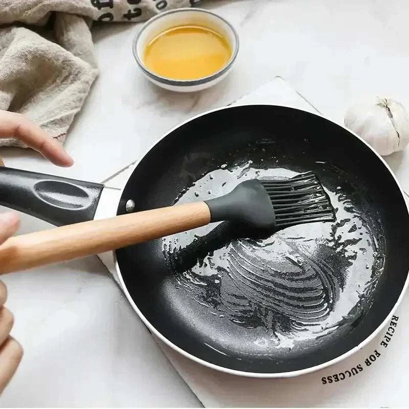 Silicone kitchen utensil with wooden handle spreading oil in a frying pan, ideal for non-stick cooking.