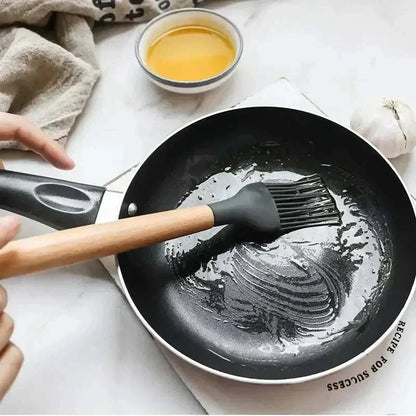 Silicone kitchen utensil with wooden handle spreading oil in a frying pan, ideal for non-stick cooking.